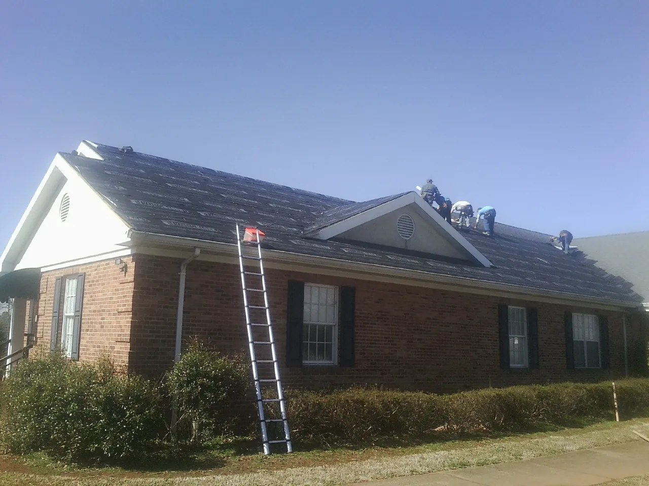 Crew tearing shingles off a brick ranch roof with a ladder set — Metal Roof Repair work by our crew in Port Orange