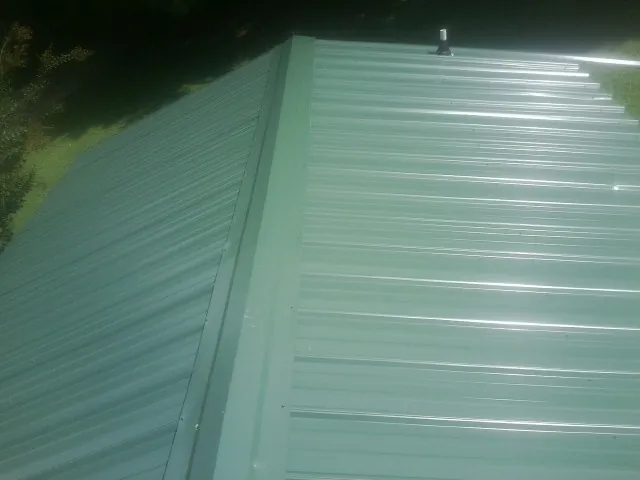 New green metal panels meeting at the ridge of a roof — Flat Roof Repair work by our crew in Port Orange