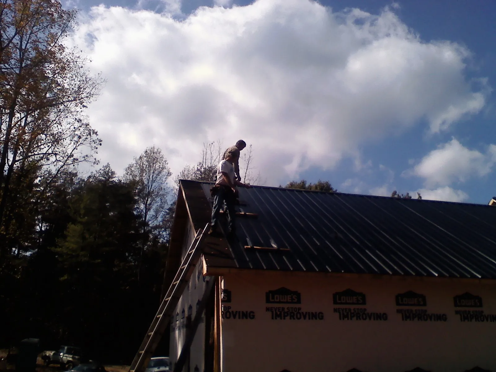 Roofer fastening dark metal panels high against a cloudy sky, from a Roof Inspection job in Port Orange