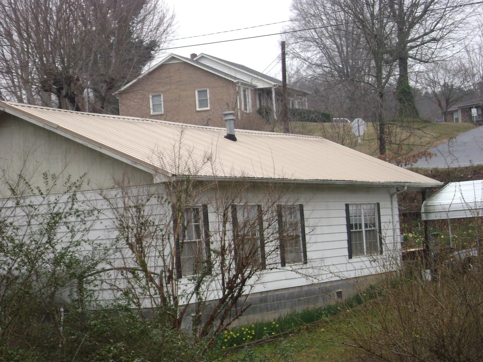 Tan metal roof on a white sided house set into a hillside — Commercial Roofing by Roofing Brothers in Port Orange